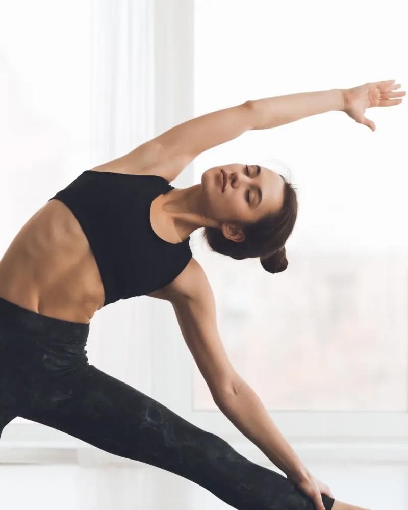 Femme en étirement latéral, le bras tendu au-dessus de la tête et les yeux fermés, dans un studio blanc lumineux